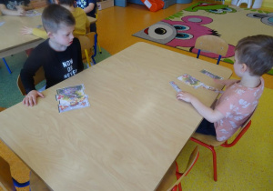 Dwóch chłopców siedzi przy stole i składa z części obrazek łąki.
